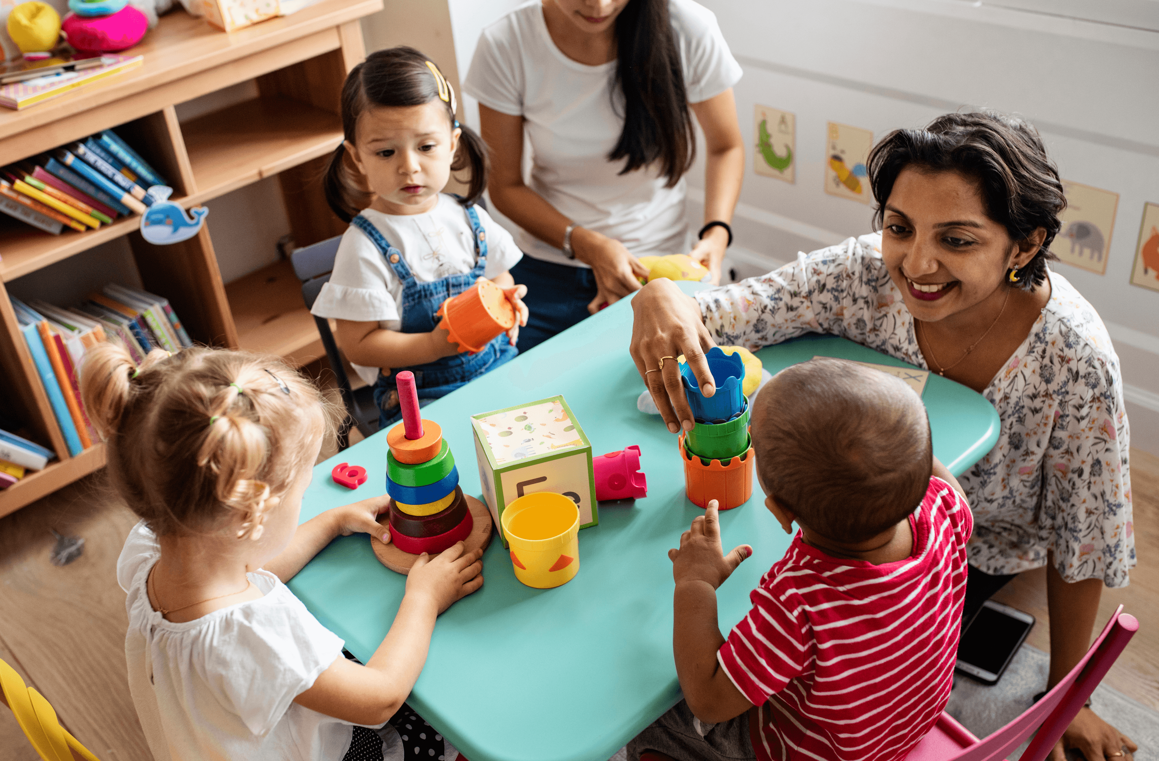 Toddlers building blocks on a table with 2 adults